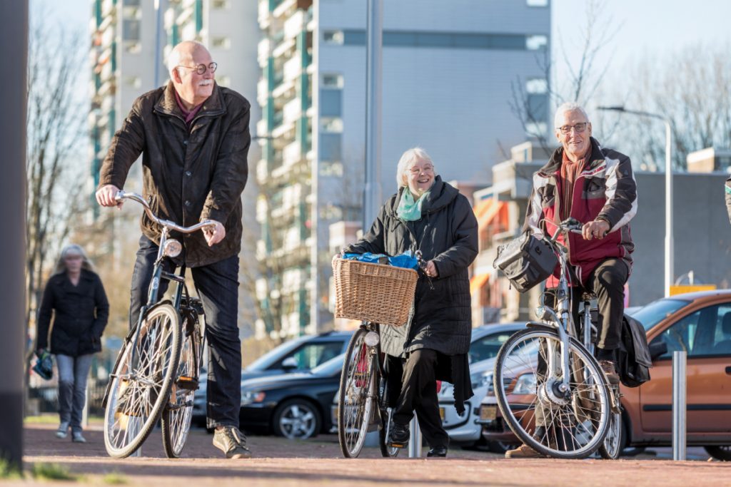 Foto van drie senioren die veilig staan te wachten op de stoep met hun fietsen in de hand.