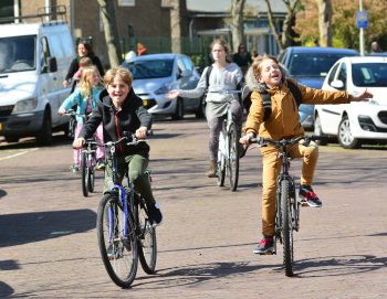 4 blije fietsende kinderen op straat.