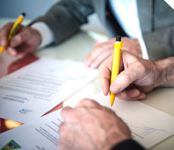 De handen van 2 bedrijfspersonen wie een pen vasthouden en op het punt staan om een document te ondertekenen.